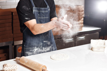 Fototapeta na wymiar Roll out the dough. expanding cloud of flour. Closeup hand of chef baker in uniform blue apron cook pizza at kitchen