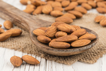 Almonds in a wooden spoon on the old white wooden table.