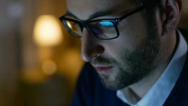 Close-up of a Man at Home Working on a Computer. He Wears Glasses, Screen Reflects in Them. Shot on RED EPIC-W 8K Helium Cinema Camera.
