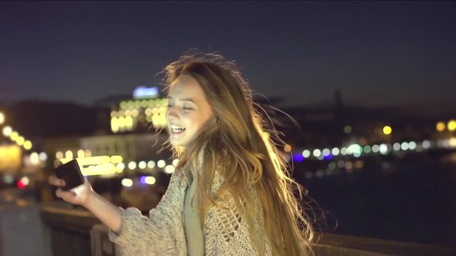 Beauty happy young girl taking picture of beautiful night city on smart phone, selfie. Beautiful young woman walking on night streets, enjoying night view. Full HD 1080p