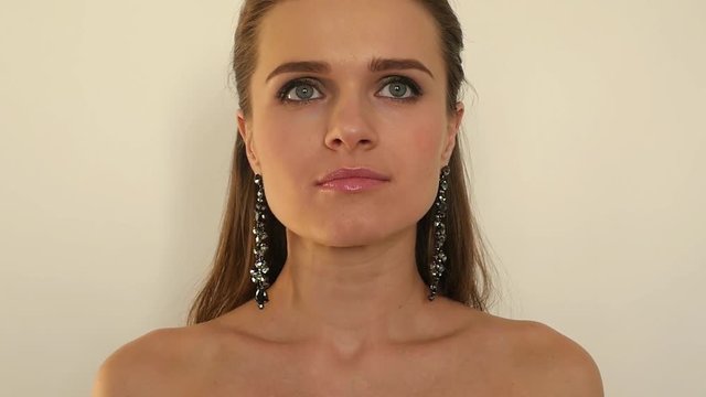 a pretty girl with long earrings is facing the camera on the shoulders with no clothes on, slow motion, 1920x1080,