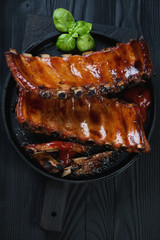 Frying pan with baked pork ribs over black wooden background