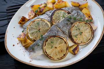 Baked sea bass fillet with potato and lemon on a plate, close-up