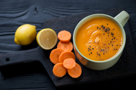 Bowl of spicy carrot cream-soup on a black wooden chopping board