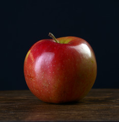 Ripe red apple on a dark wooden table on a black background.