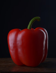 Red bell peppers on a dark wooden table on a black background.