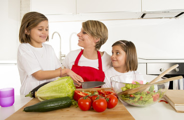young mother in cook apron and sweet beautiful twin daughters cooking preparing together salad