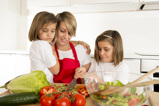 young mother in cook apron and sweet beautiful twin daughters cooking preparing together salad