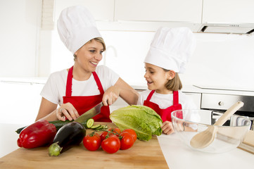 mother and little daughter cooking together with hat apron preparing salad at home kitchen
