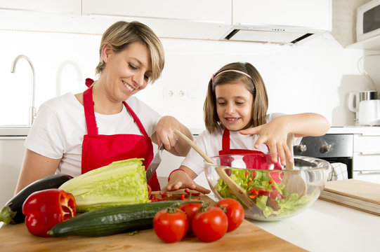 mother and little daughter cooking together with cook  apron preparing salad at home kitchen