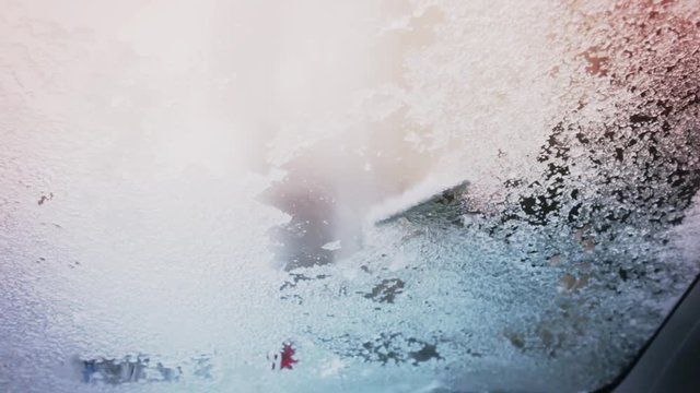 Close up shot of a person removing the ice from a car's frozen windshield, with and ice scraper.