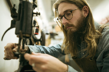 Serious shoemaker adjusting sewing machine at workshop