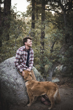 Man With Dog Looking Away While Leaning On Rock In Forest