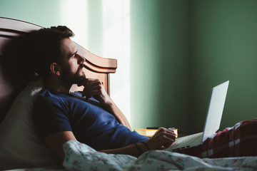 Young man lying in the bed working on a laptop