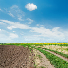 rural road in agricultural field and clouds in blue sky