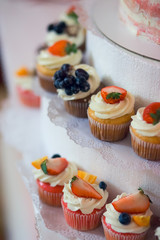 a variety of delicious cupcakes with white cream decorated with berries strawberries blueberries currants on wedding table close-up