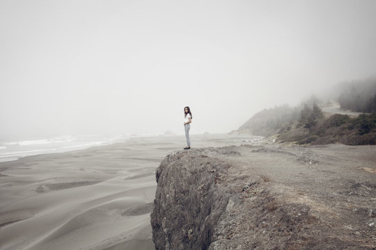 Side view of woman standing on cliff at beach during foggy weather