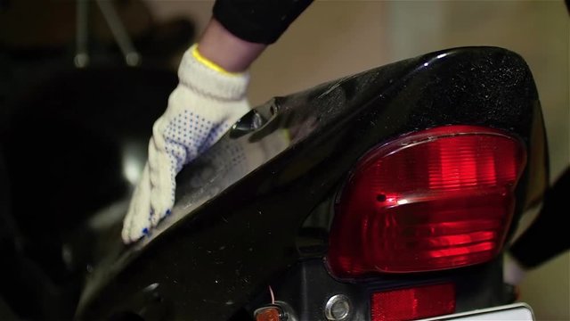 Mechanic removes plastic back tail of black motorcycle in workshop