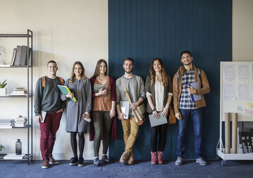Portrait of friends standing against wall in classroom