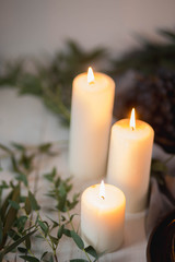 beautiful white burning candles close-up decorated with green eucalyptus leaves on white wooden background