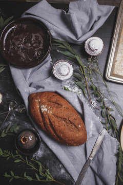 rye black bread oblong shape on the table with the cupcakes and brown ceramic plates on gray blue towel on black wooden background close-up food photos