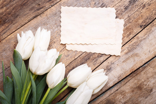 Vintage paper card with white tulips on wooden background. Invitation card with flowers on wood