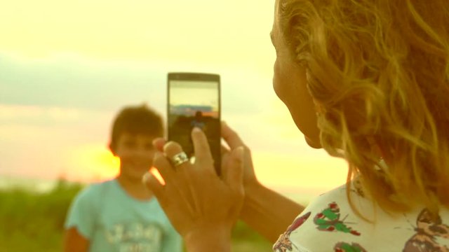 Happy family mother with her little son taking selfies with smartphone outdoors. Posing and smiling, enjoying nature. Vacation concept. Slow motion 240 fps, high speed camera. Full HD 1080