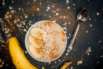 Smoothie with yogurt, banana and oatmeal, idea for a wholesome healthy breakfast. On a dark gray concrete stone background, with ingredients for cooking. Copy space