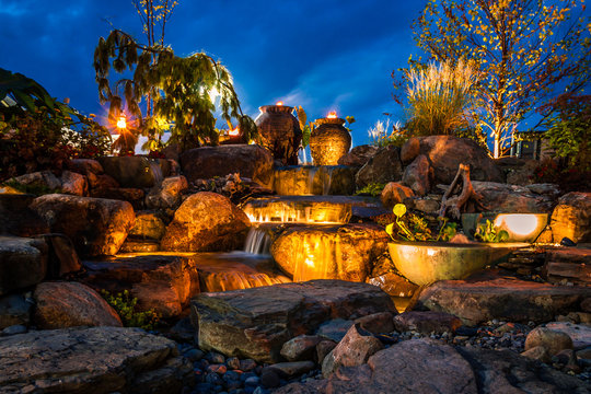 Waterfall Fountain Landscape At Night With Gold Color Lights And Tiki