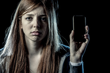 worried teenager holding mobile phone as internet addict and victim of cyber bullying