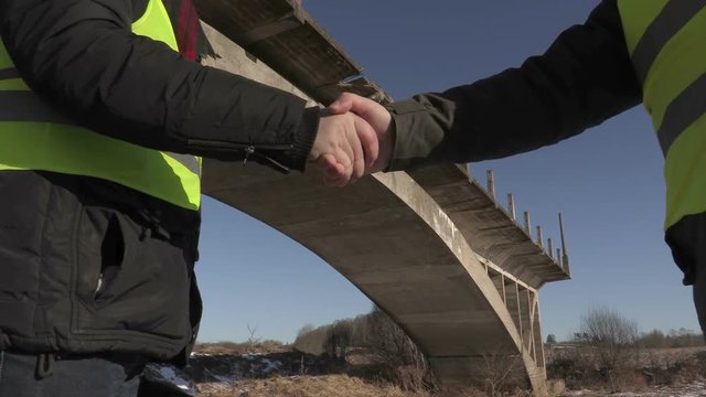 Engineers shaking hands near unfinished bridge