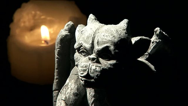 Multiple lit candles adjacent a figurine or statuette of a gargoyle.