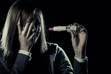 young sad pregnant woman or female teenager scared and shocked holding pregnancy test positive result