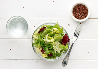 Mixed salad in glass bowl with flax seed and water on white wooden table. - 136488185
