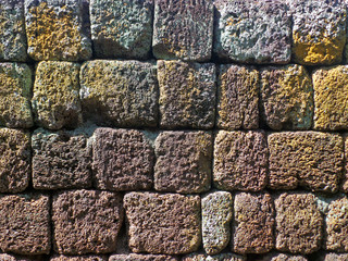 Texture of dark shade of brown and yellow rough ancient stone wall in the sunlight 