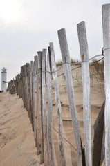 White lighthouse at the end of the wooden fence on the sandy bea