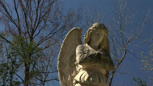 Camera moves to reveal a winged celestial image captured in stone adorning a gravesite.