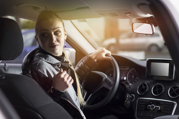 Beautiful woman backing up her car from the parking lot. Smiling young woman driving her car. Lens flare in background.