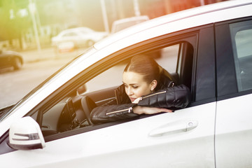 Naklejka premium Szczęśliwa uśmiechnięta młoda kobieta siedzi w samochodzie. Oparty o szybę samochodu. Piękna niebieskooka kobieta w swoim samochodzie. Flara obiektywu w tle.