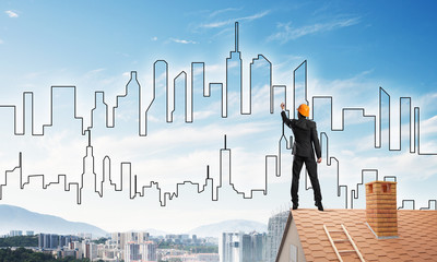 Man architect draw silhouette of modern city on blue sky. Mixed media
