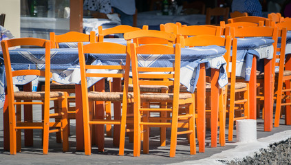 Fototapeta na wymiar Orange wooden tables at traditional Greek tavern on Santorini island, Greece