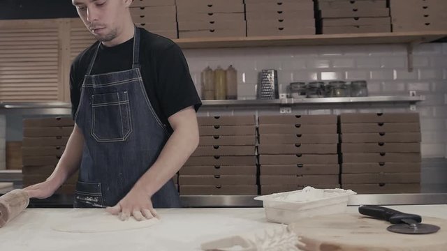 Pizza maker chef is cooking dough at commercial kitchen in moder restaurant for pizza delivery