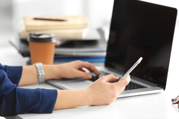 Young woman with laptop and mobile phone in office, closeup