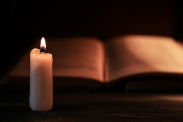 Burning candle and Bible on wooden table