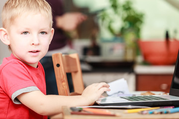 Little boy with laptop on table in home.