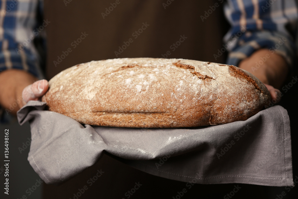 Wall mural male hands holding freshly baked rye bread, closeup