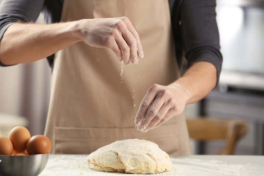 Man sprinkling flour over fresh dough on kitchen table