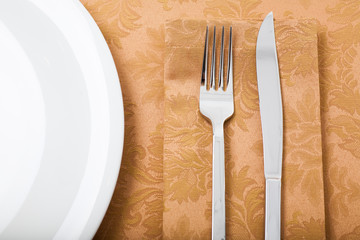 top view of empty plate with fork and knife on a goldish tablecloth