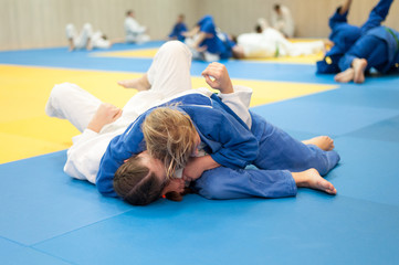 Unrecognizable female judoka in blue judo gi keeps the opponent in the hold down