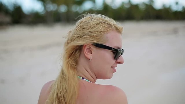 Young blonde woman in bikini walking on the beach